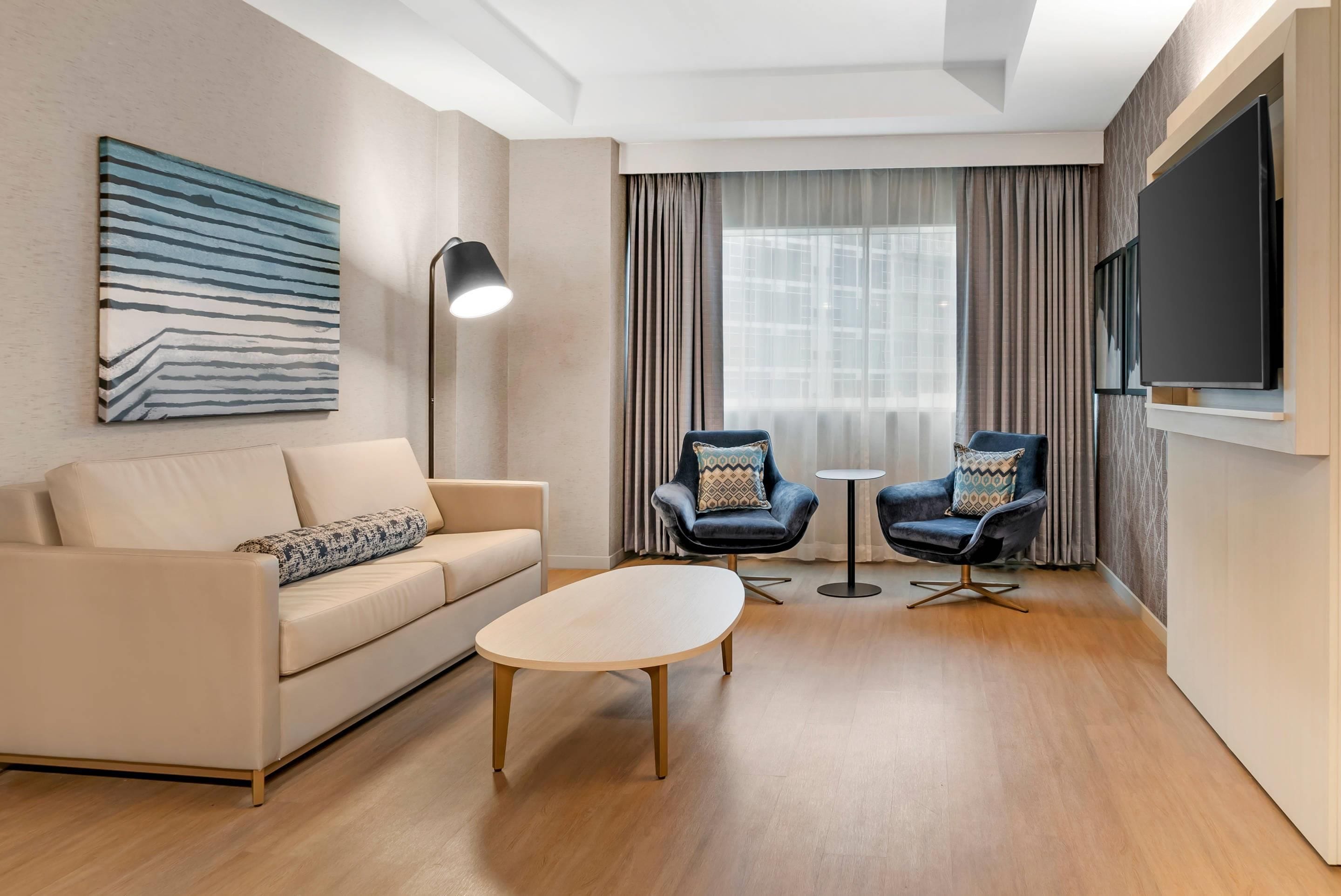 A modern living room with a sofa, two armchairs, a coffee table, a floor lamp, and a TV mounted on the wall.