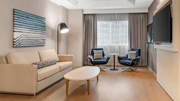 A modern living room with a sofa, two armchairs, a coffee table, a floor lamp, and a TV mounted on the wall.