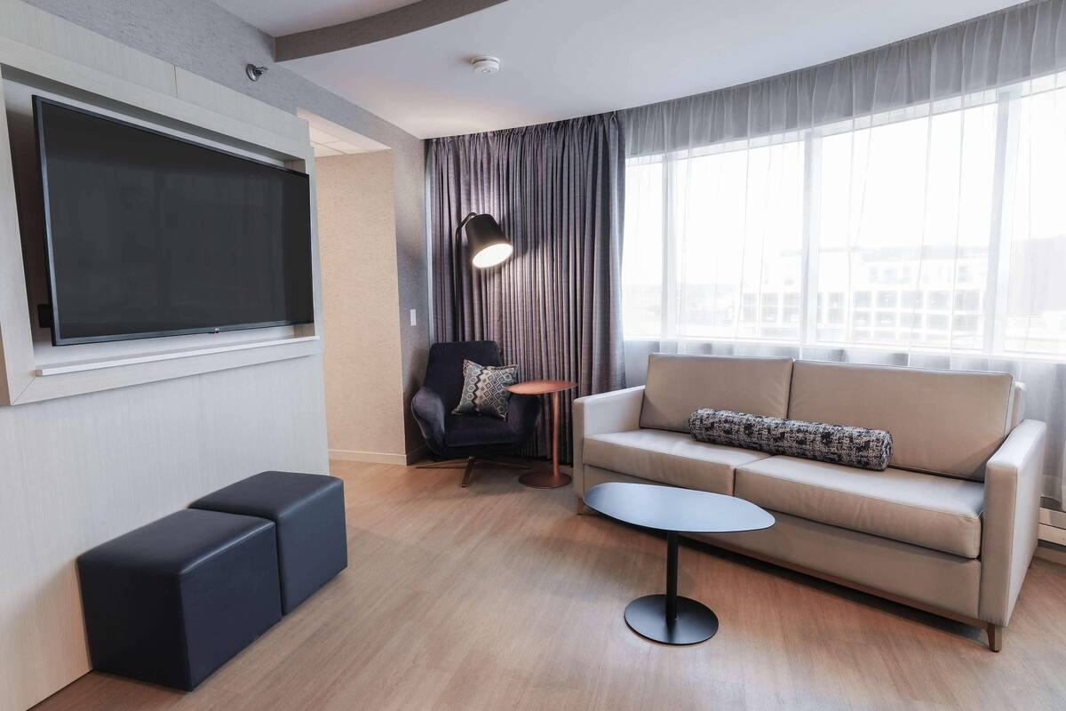 Una sala de estar moderna con un televisor de pantalla plana grande, un sofá, una mesa de centro y una silla.