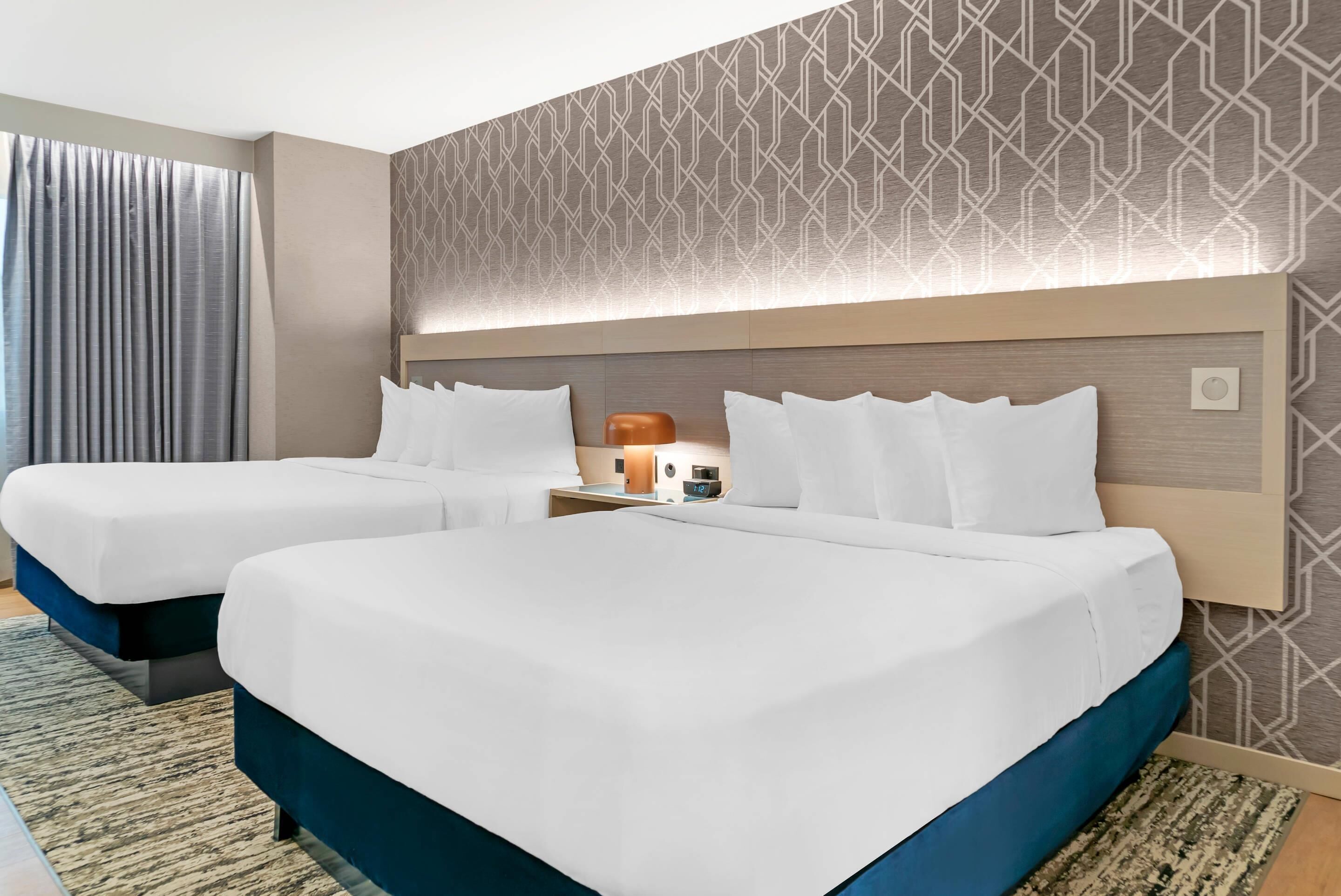 A hotel room with two beds, a nightstand with a lamp, and a patterned wall.