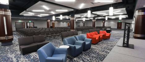 Un salón de conferencias con filas de sillas, un escenario y zonas de estar con sofás y sillones.