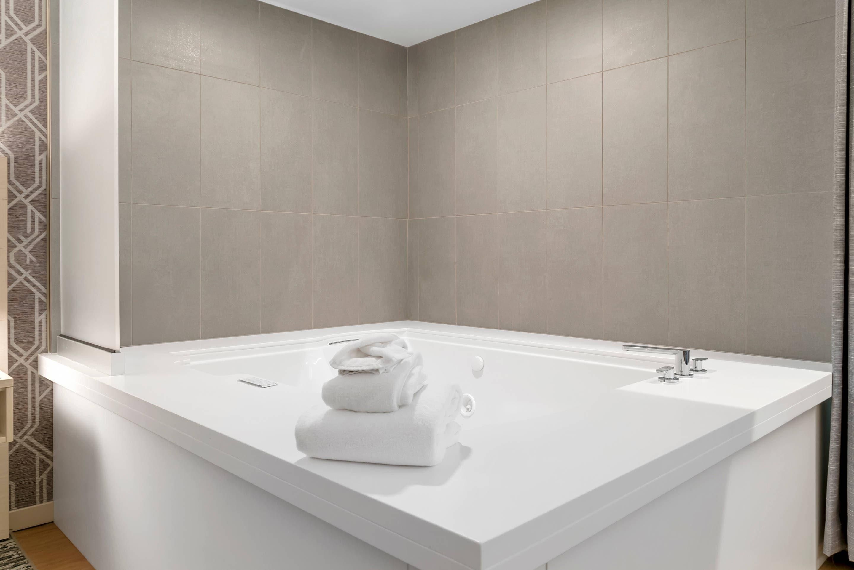 A modern bathroom with a large white bathtub, a white sink, and a towel stack.