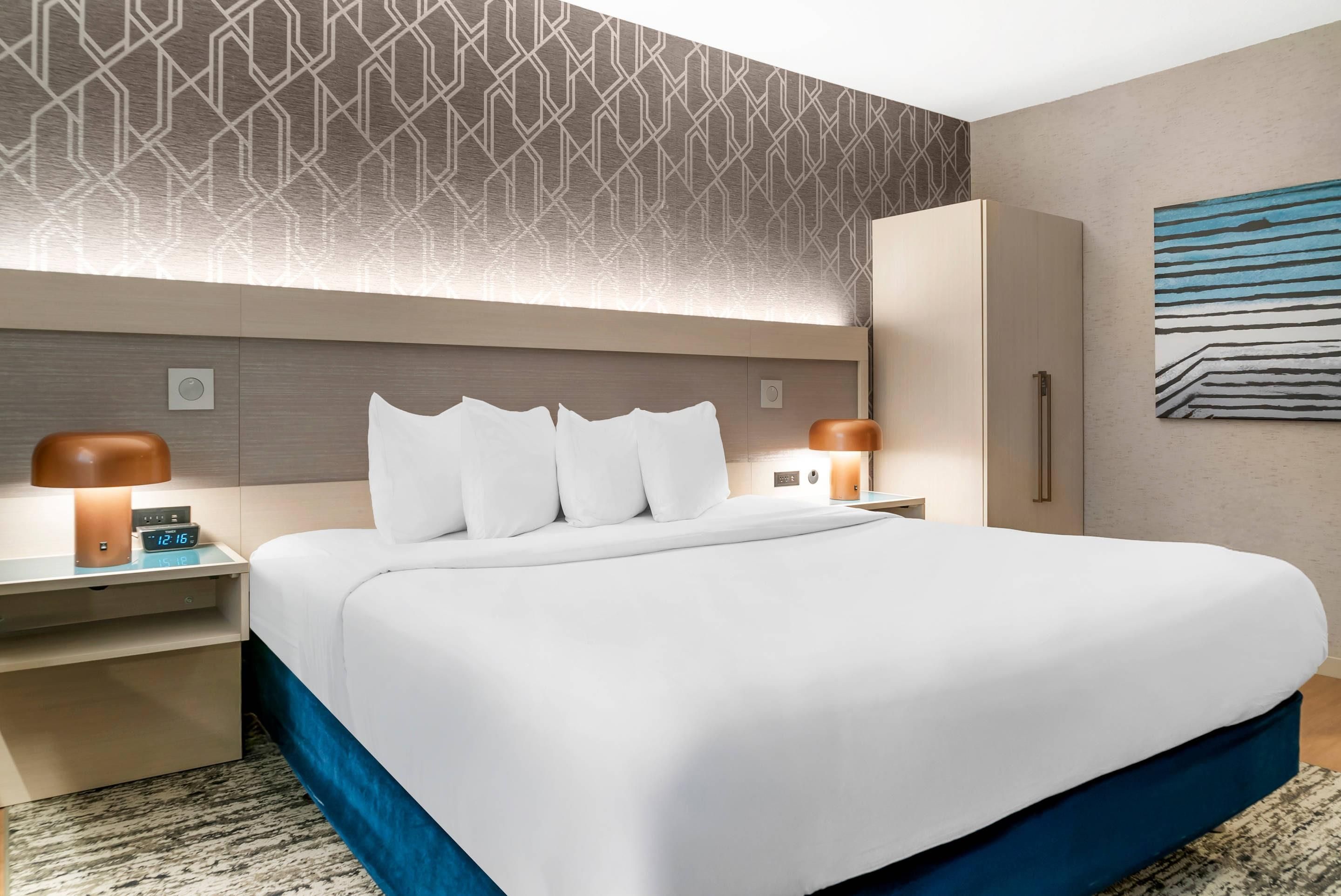 Une chambre d’hôtel avec un grand lit, deux tables de chevet, une armoire et un mur décoré d’un motif.