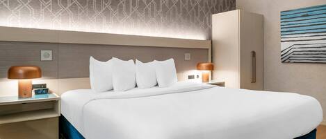 Une chambre d’hôtel avec un grand lit, deux tables de chevet, une armoire et un mur décoré d’un motif.