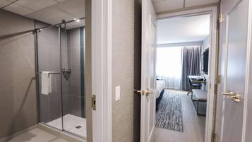 A hotel room with a glass-enclosed shower, a bed with a view, a desk, and a television.