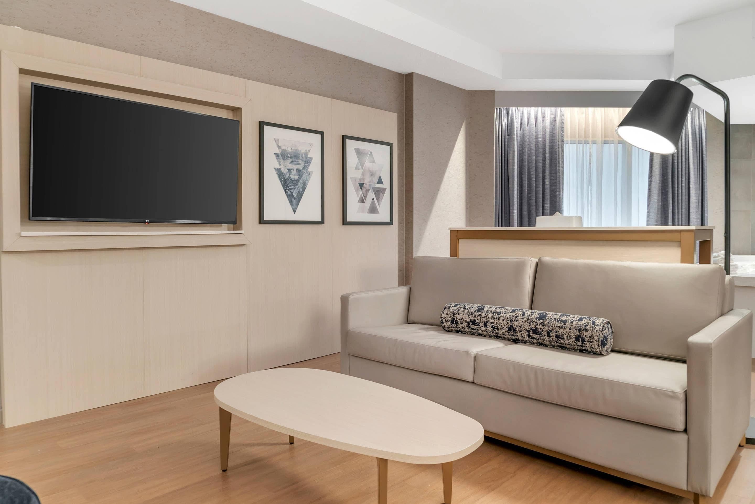 A modern living room with a flat-screen TV, a sofa with a patterned pillow, a small table, and a floor lamp.