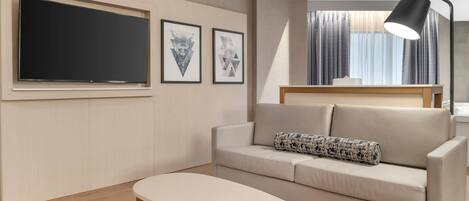 A modern living room with a flat-screen TV, a sofa with a patterned pillow, a small table, and a floor lamp.