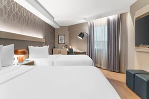 A hotel room with two beds, a desk, a chair, a TV, and a large window with curtains. - Radisson Plaza Hotel at Kalamazoo Center (Kalamazoo)
