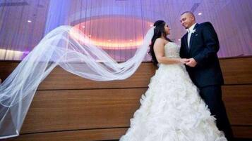A wedding couple in a room with a draped curtain backdrop and a patterned carpet.