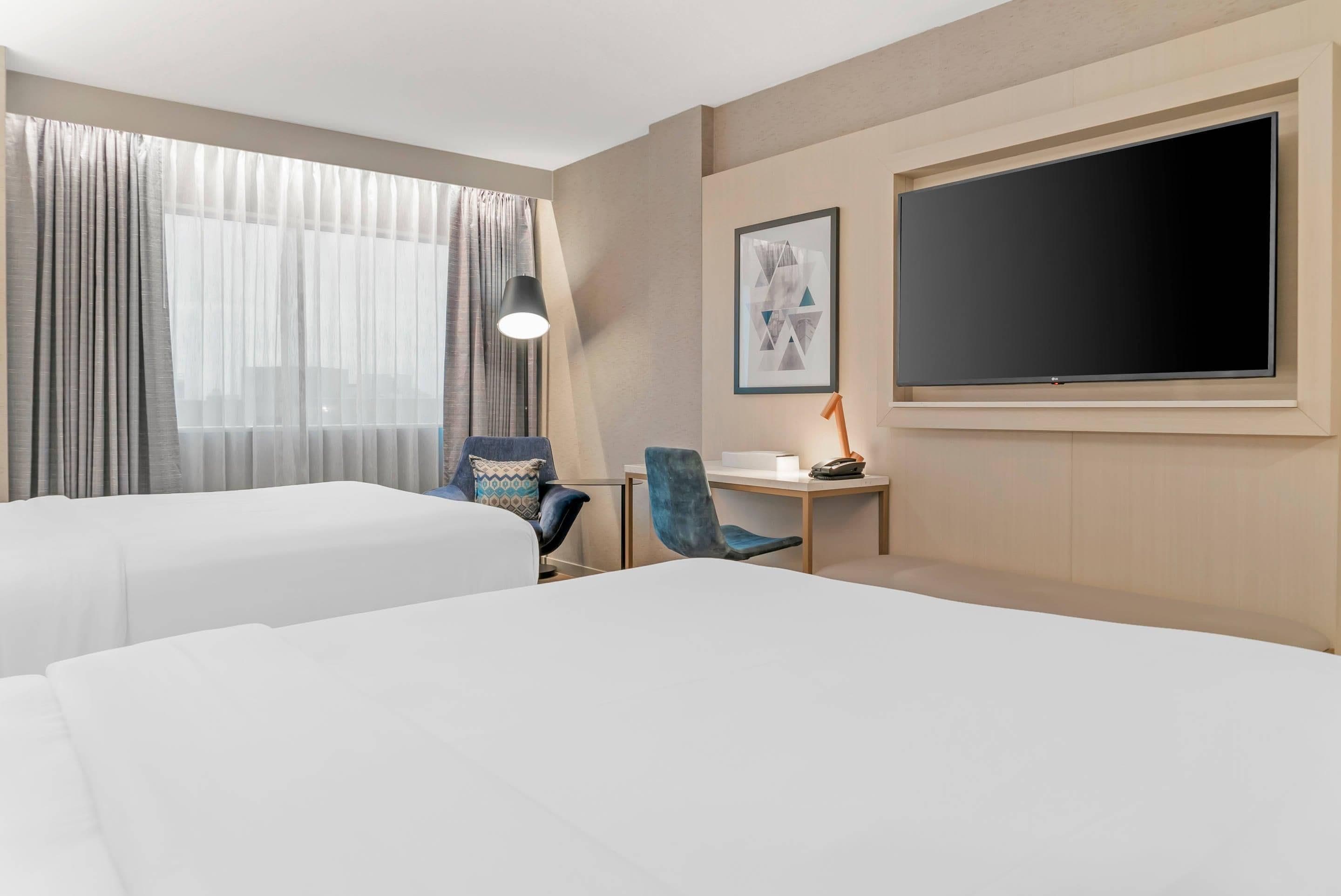 A hotel room with two beds, a desk, a chair, a TV, and a window with curtains.