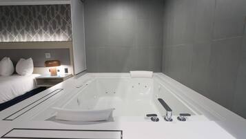 A modern bathroom with a large bathtub, a white sink, and a bedside table with a lamp.