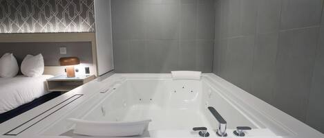 A modern bathroom with a large bathtub, a white sink, and a bedside table with a lamp.