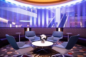 Un vestíbulo de hotel moderno con una mesa redonda, cuatro sillas azules y un jarrón decorativo.