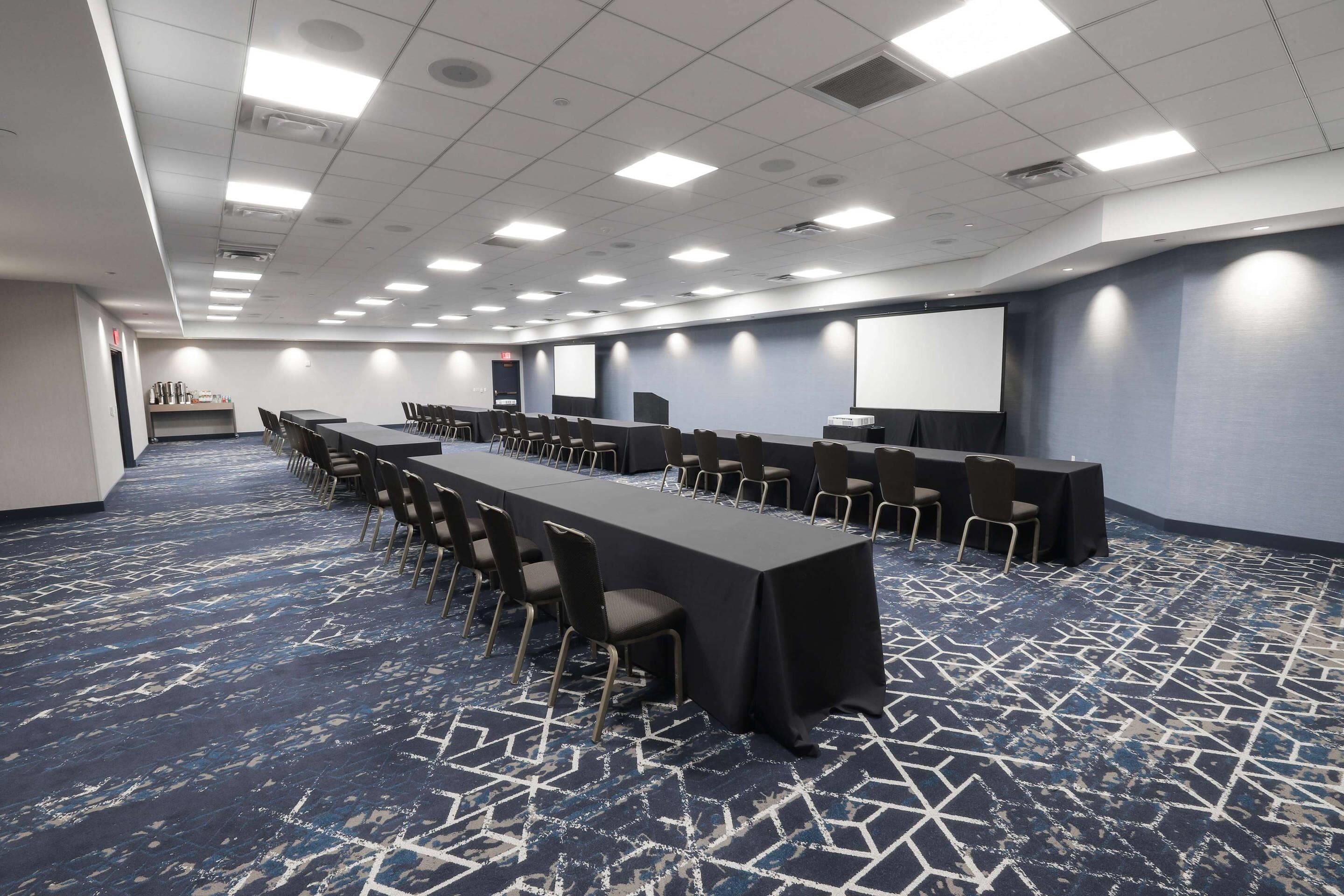 A conference room with a long table, chairs, a projector screen, and a carpeted floor.