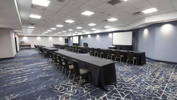 A conference room with a long table, chairs, a projector screen, and a carpeted floor.