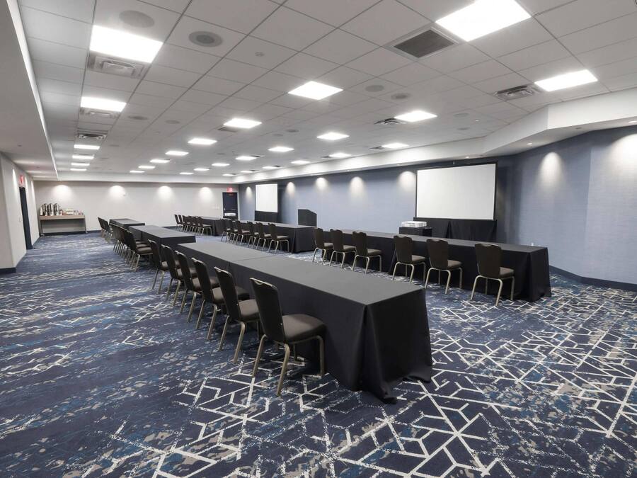 A conference room with a long table, chairs, a projector screen, and a carpeted floor.