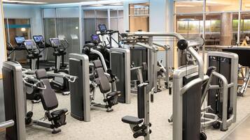 Un gimnasio con diversas máquinas de ejercicio, ventanas amplias y vistas al exterior.