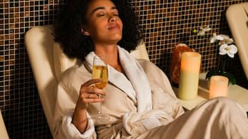 A person relaxing in a chair with a glass of wine, surrounded by candles and an orchid.