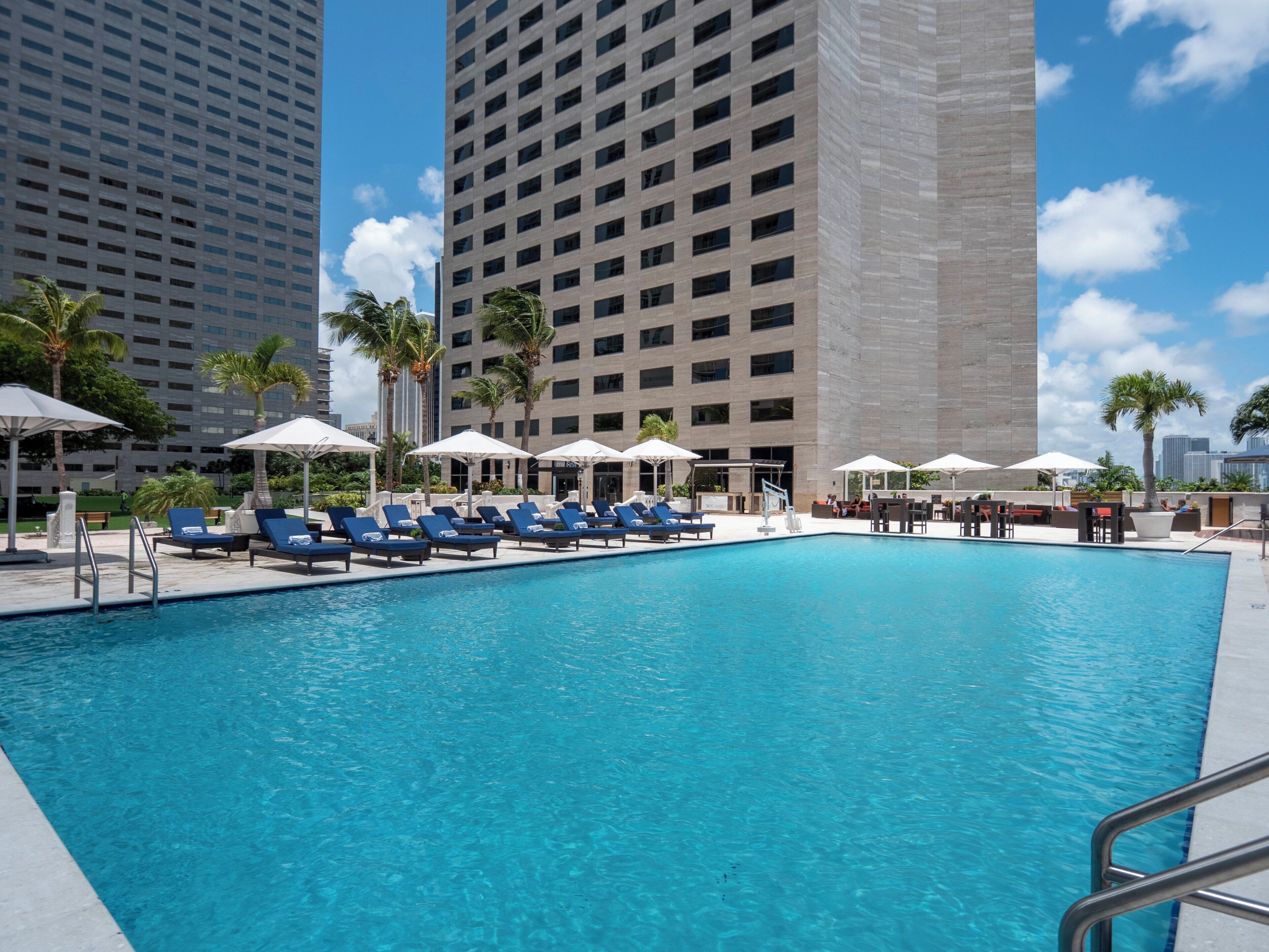 Une piscine entourée d’immeubles imposants, avec des chaises longues et des parasols.