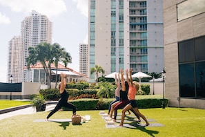 A group of people doing yoga on mats in an outdoor area with a cityscape in the background.