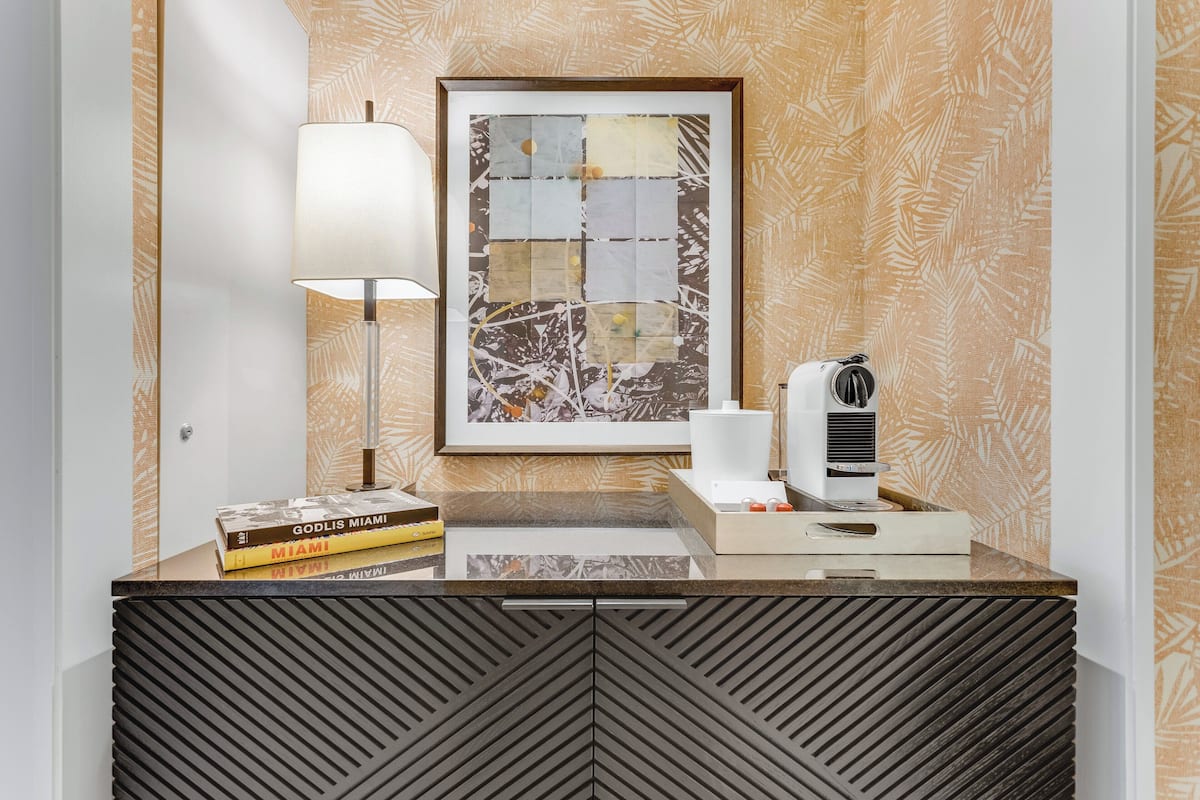 A modern hotel reception desk with a framed abstract artwork, a lamp, a coffee machine, and a few books.