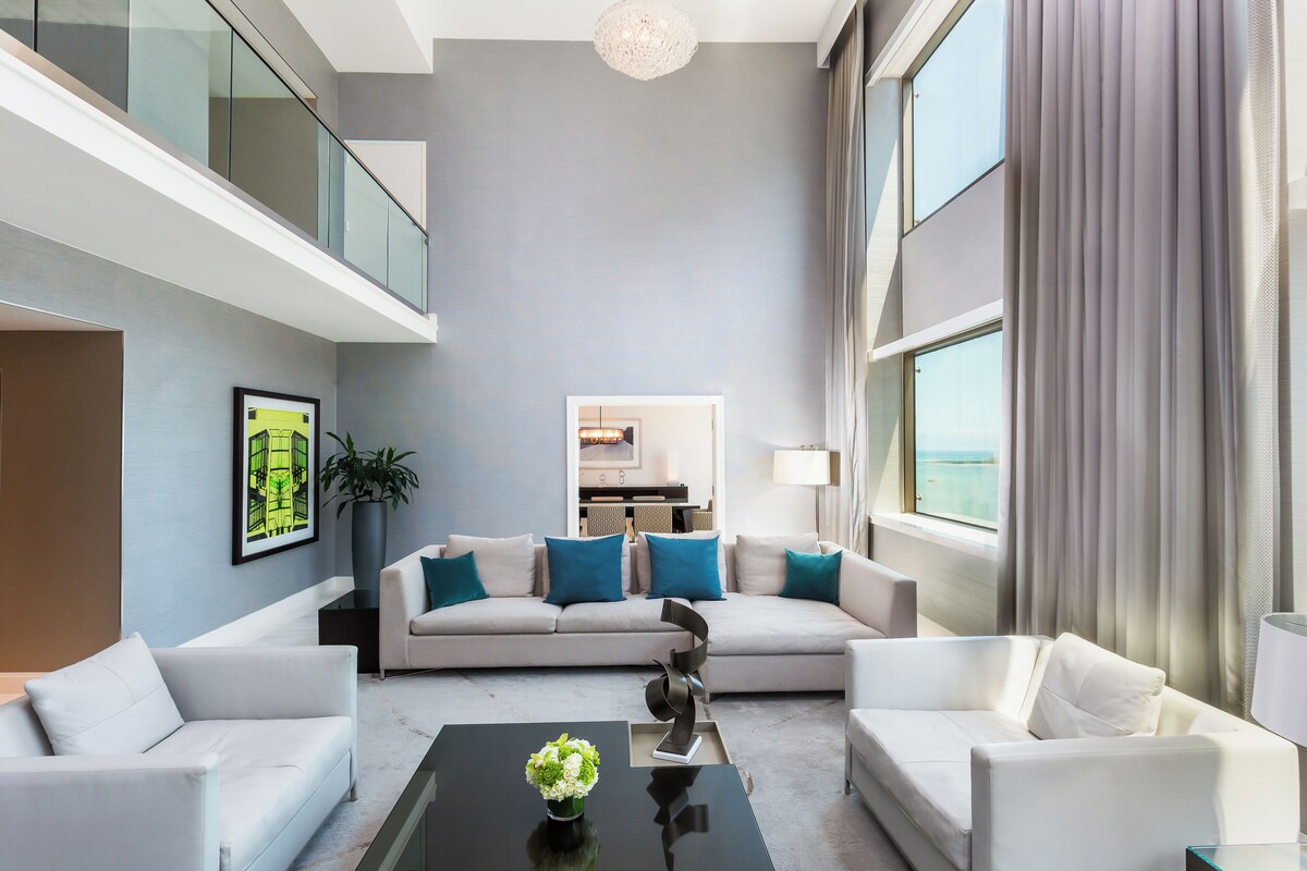 A modern living room with a sofa set, a coffee table with a vase, and a view of the sea through large windows.