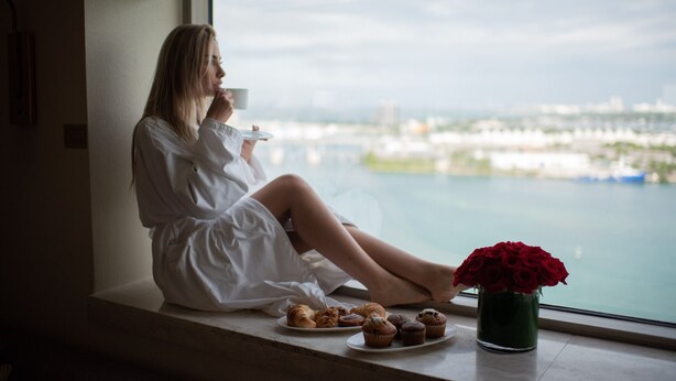 A person sitting by a window with pastries and a vase of flowers on the windowsill.
