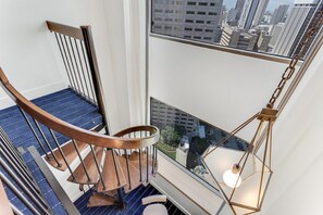 A modern staircase with a wooden handrail and metal balusters, leading to a balcony with a city view.