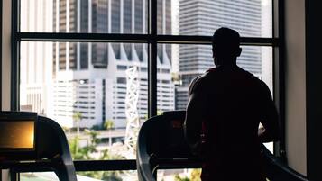 A person running on a treadmill inside a room with large windows overlooking a cityscape.