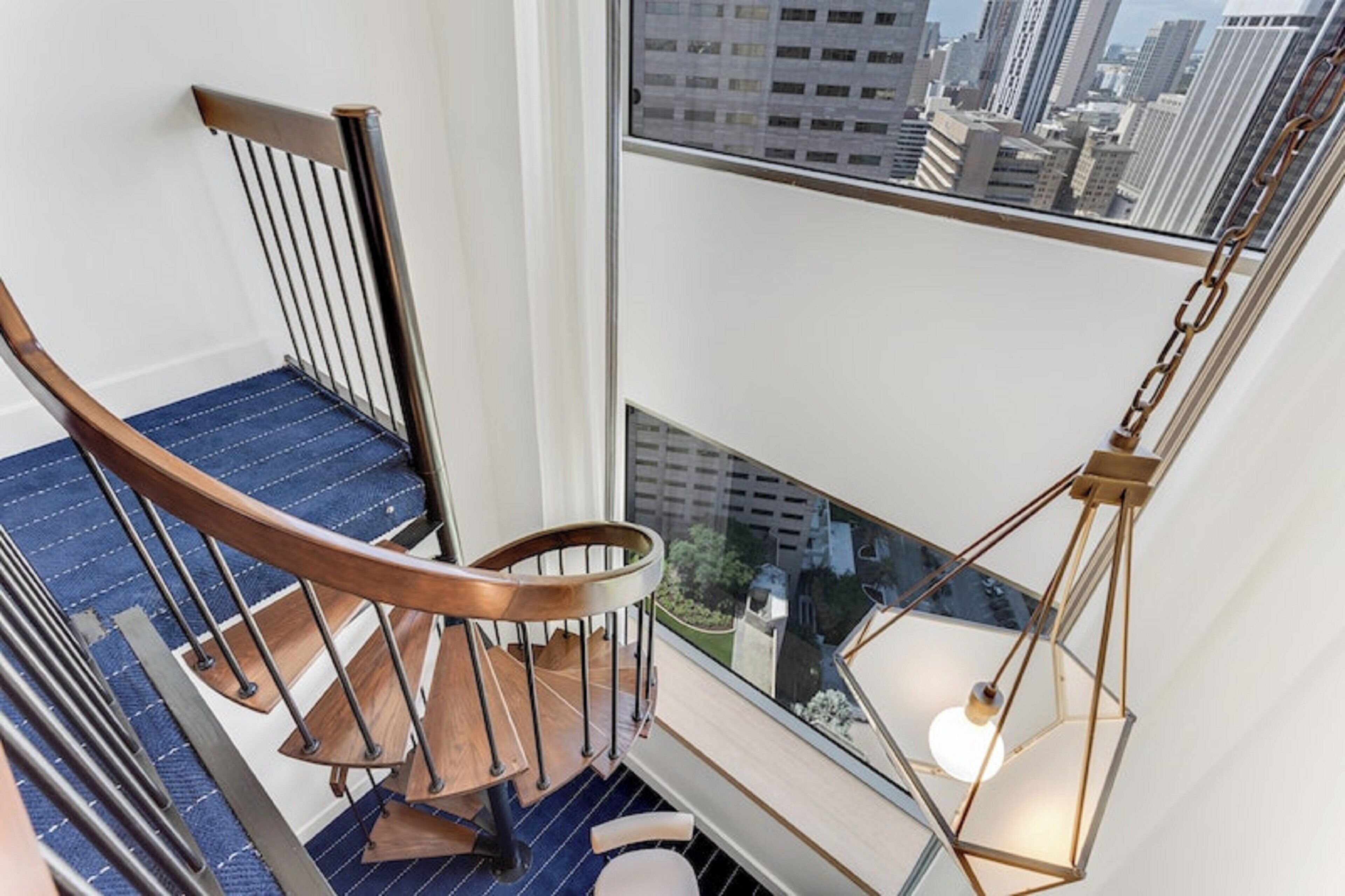 Una scala a chiocciola con gradini in legno e ringhiere in metallo, che conduce a un balcone con vista sulla città.