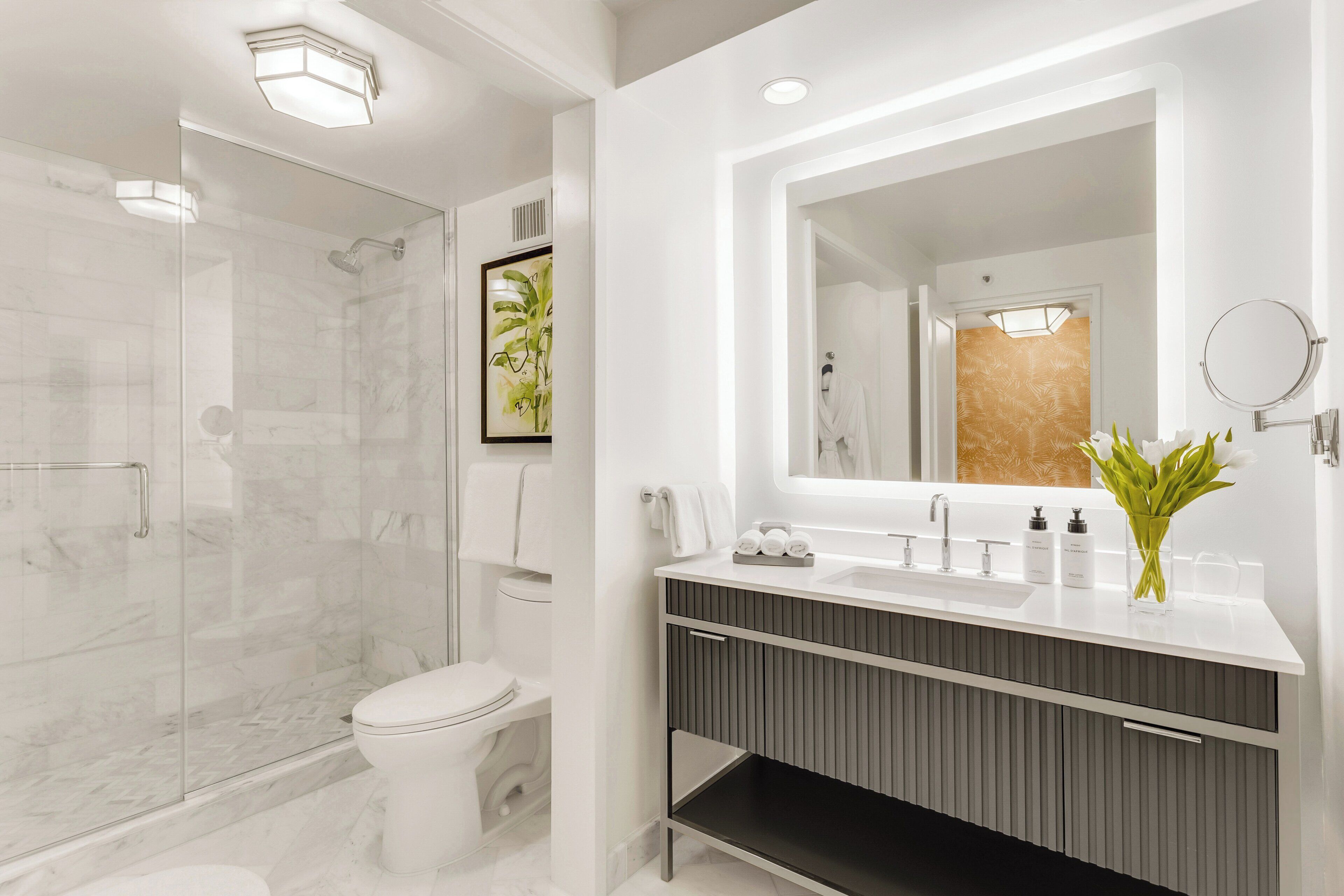 A modern bathroom with a glass shower enclosure, a toilet, a vanity with a large mirror, and a sink with toiletries.