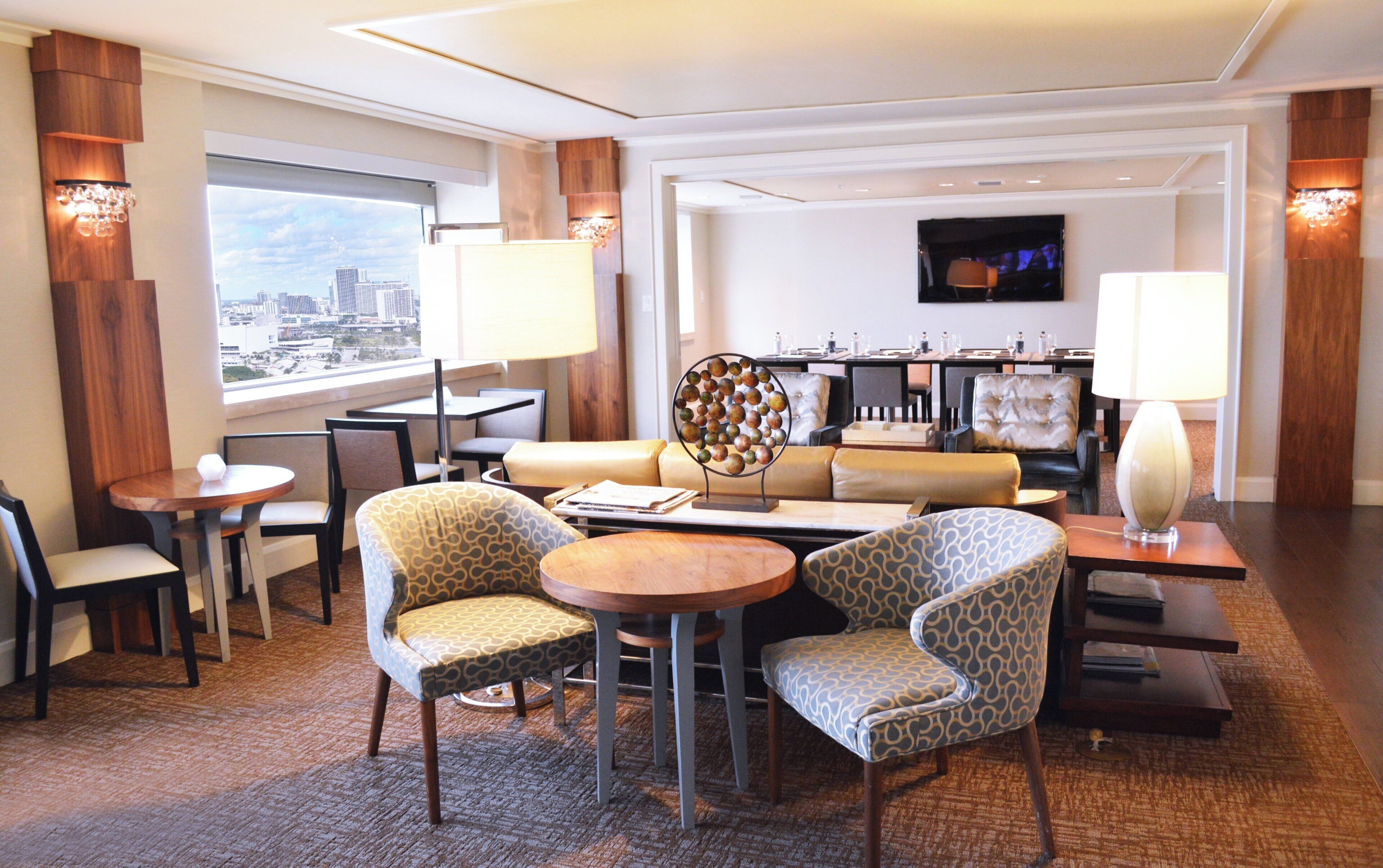 A hotel room with a seating area, a dining table, and a television mounted on the wall.
