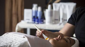 A person lying down with a medical device on their face, possibly a treatment or examination, in a room with a table in the background containing various bottles and containers.