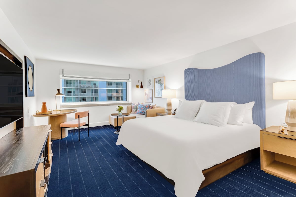 A hotel room with a large bed, a desk, a chair, a small table, and a window.