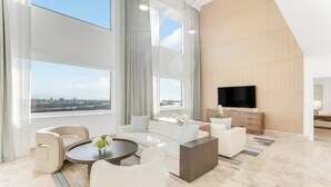 A modern living room with a large TV, comfortable seating, and large windows offering a city view.
