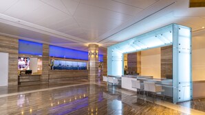 A modern hotel lobby with a polished marble floor, a reception desk, and a seating area with white chairs.