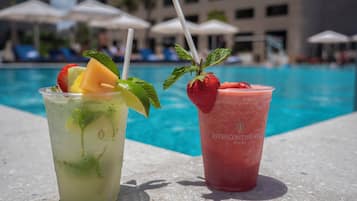 Two drinks by a poolside with umbrellas and lounge chairs in the background.