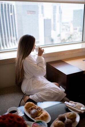 A person sitting by a window with a city view, a table with pastries, and a cup of coffee. - InterContinental Miami by IHG (Miami)