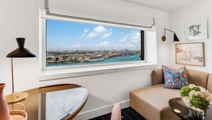 A modern living room with a large window overlooking a cityscape, a sofa with a patterned cushion, a side table with a vase of flowers, and a floor lamp. - InterContinental Miami by IHG (Miami)