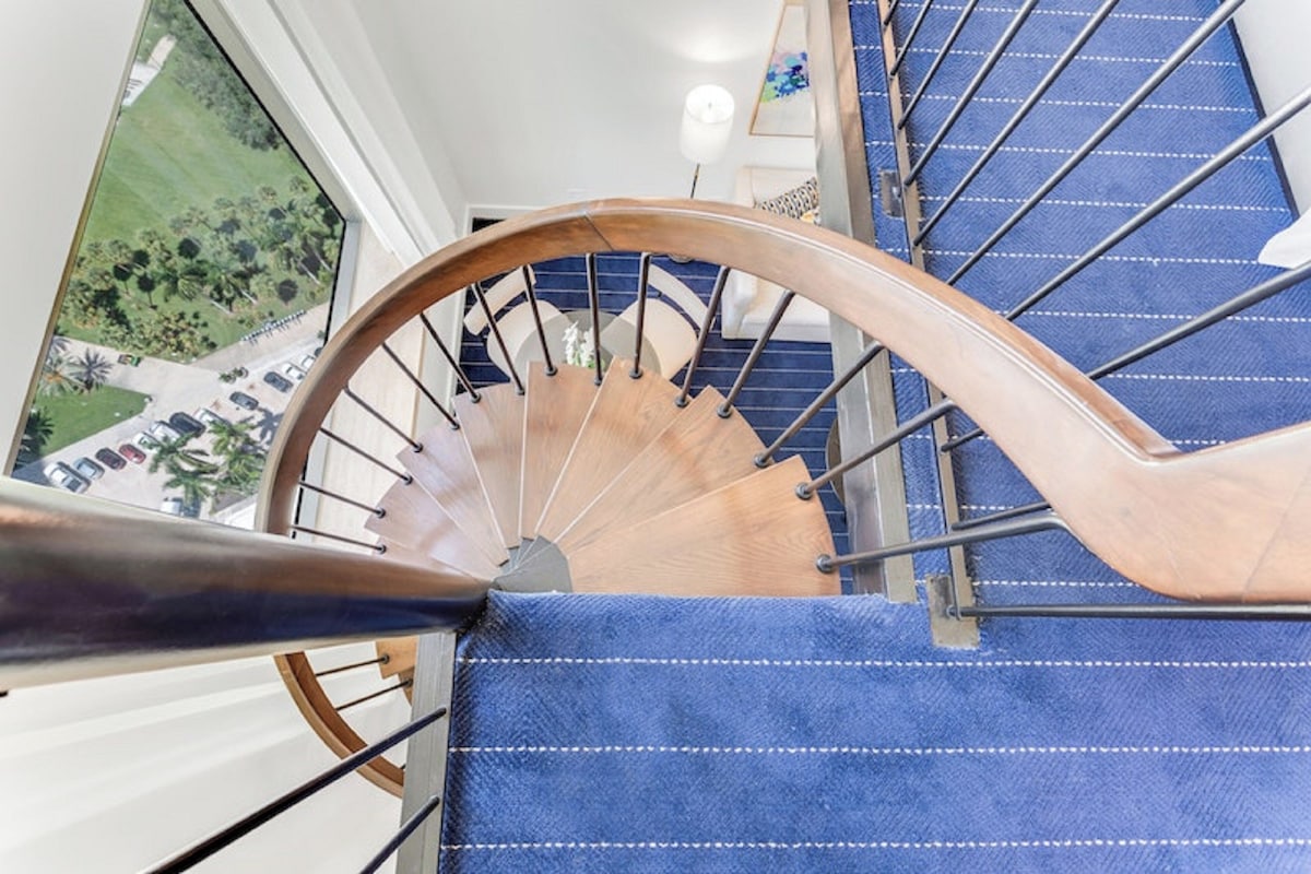 A wooden spiral staircase with blue carpeted steps and metal railings.