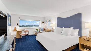 A hotel room with a large bed, a desk, a chair, a TV, and a window with a city view.