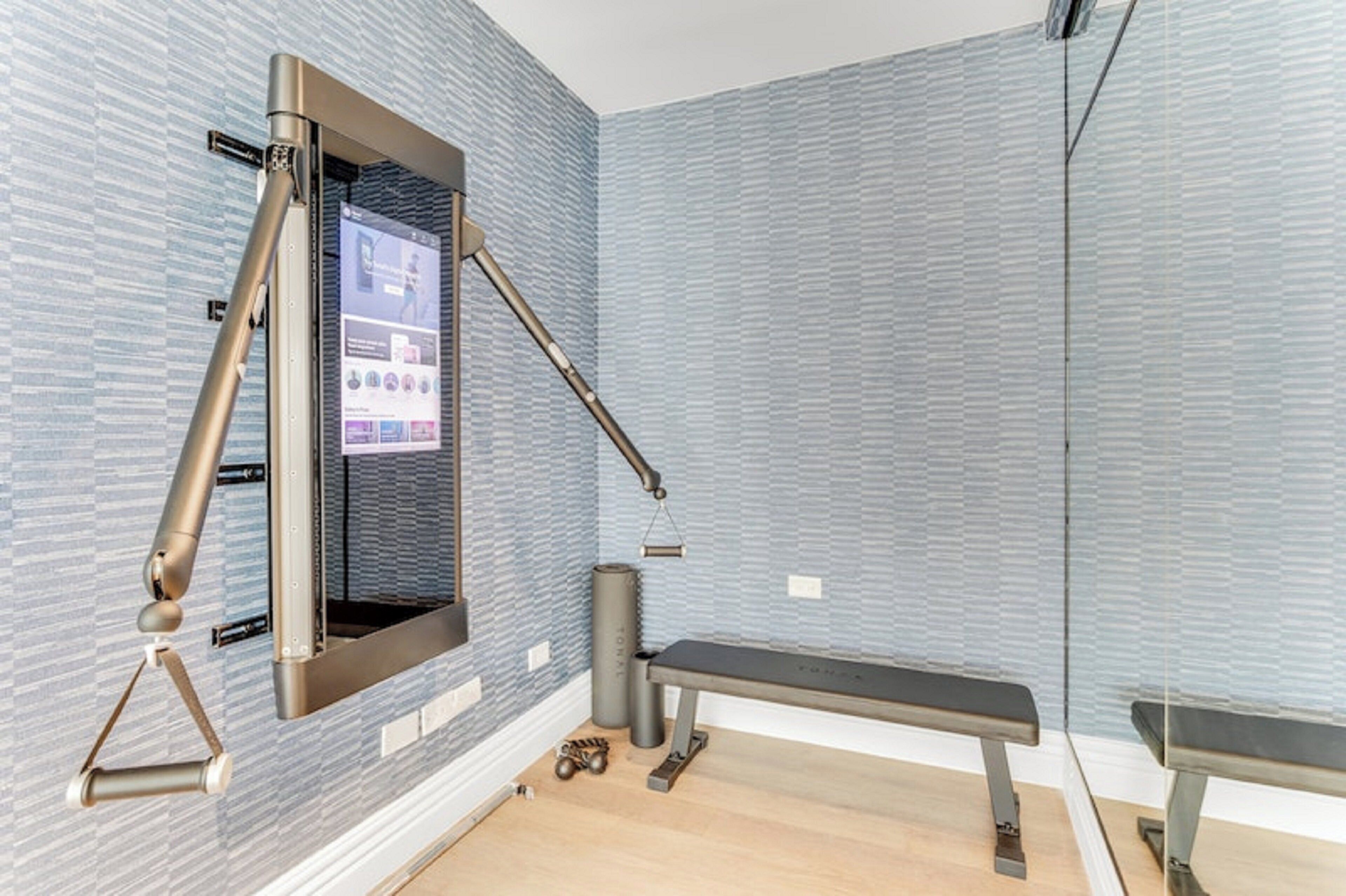 Ein modernes Fitnessstudio mit Wandbildschirm, einer Bank und Trainingsgeräten.