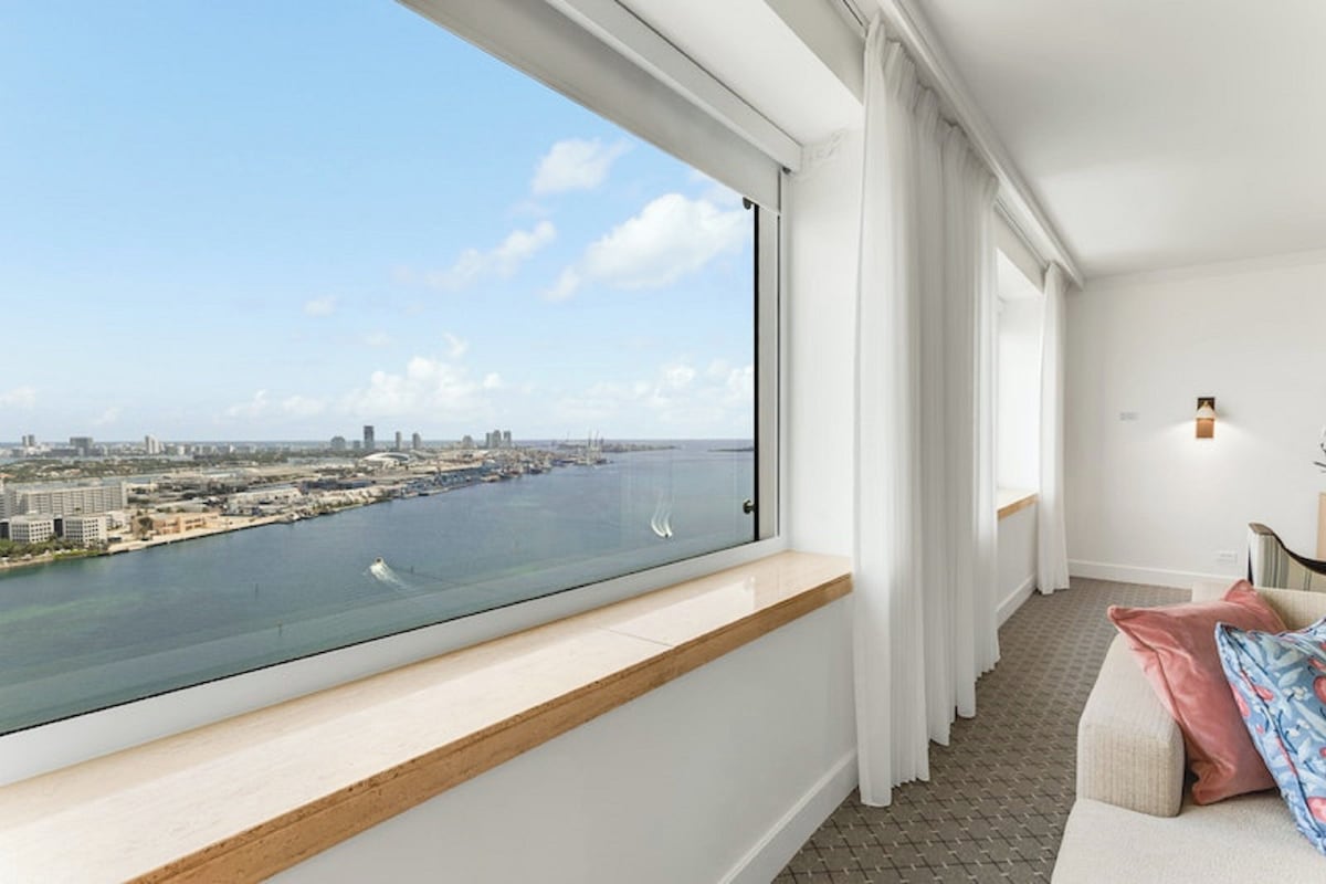 A modern hotel room with a large window overlooking a cityscape and water.