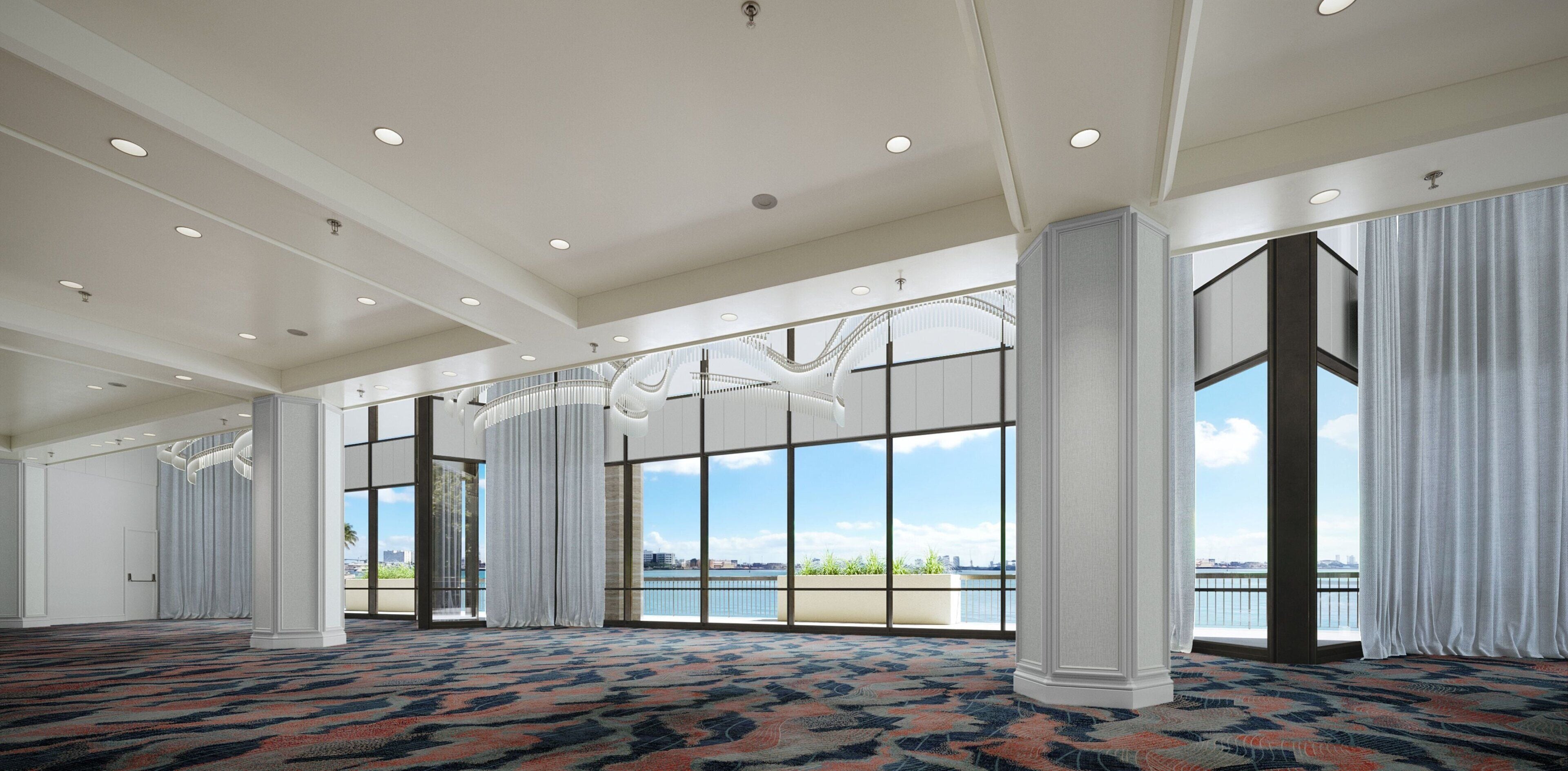 A spacious hotel room with large windows, a patterned carpet, and a view of the water.
