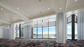 A spacious hotel room with large windows, a patterned carpet, and a view of the water.