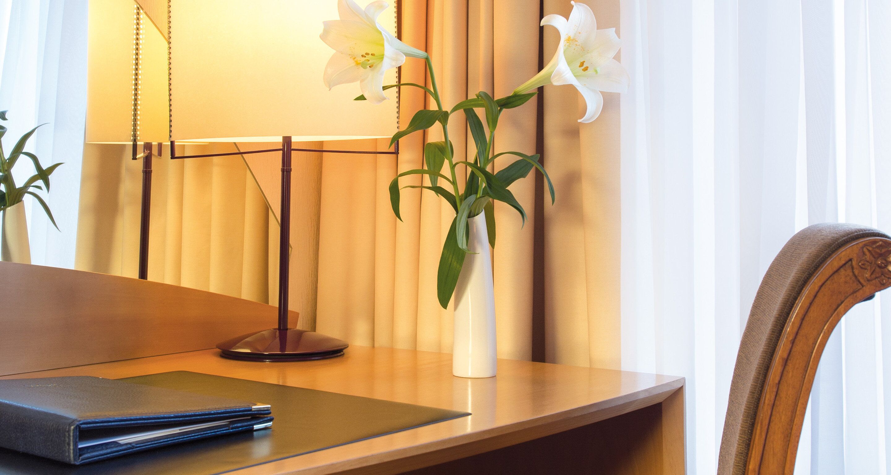 Een bureau met een laptop, een vaas met bloemen en een lamp in een hotelkamer.