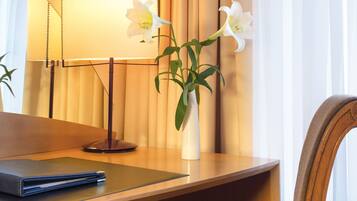 Een bureau met een laptop, een vaas met bloemen en een lamp in een hotelkamer.