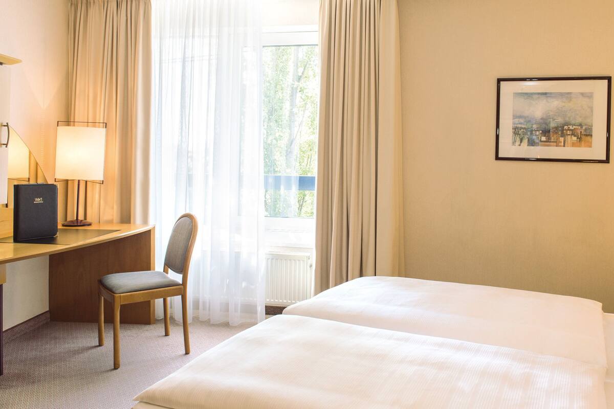 Une chambre d’hôtel avec un lit, un bureau avec une chaise, une lampe et un tableau encadré au mur.