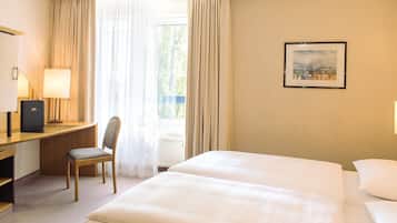 Habitación de hotel con cama, escritorio, silla, lámpara y un cuadro en la pared.