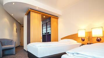 Habitación de hotel con dos camas, una silla, un armario y dos lámparas fijadas a la pared.